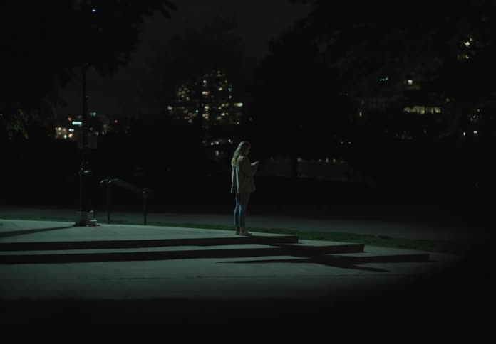 A teenager stands on a street corner and uses her cell phone
