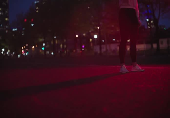 A white woman stands on a court in a park bouncing a ball