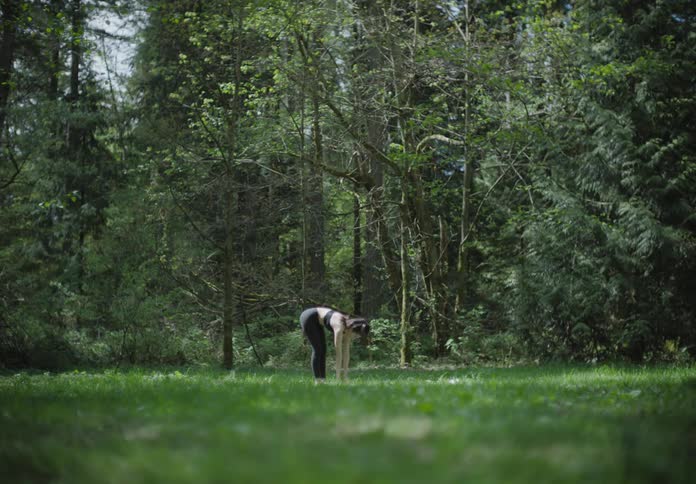 A woman in a grassy field stretching with trees in the background