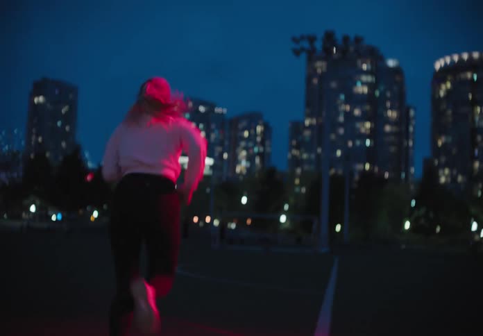 A woman runs across a court at night by a large lit city