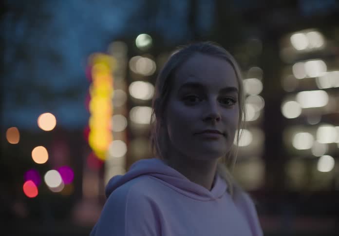 A white female teenager stands outdoors in the city