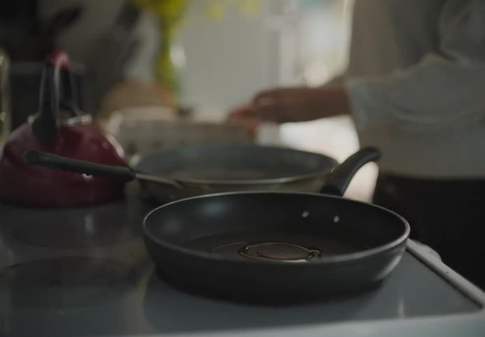 Female drizzles olive oil into a frying pan on a flat top electric stove removes an egg from the carton and cracks it into the frying pan to start cooking