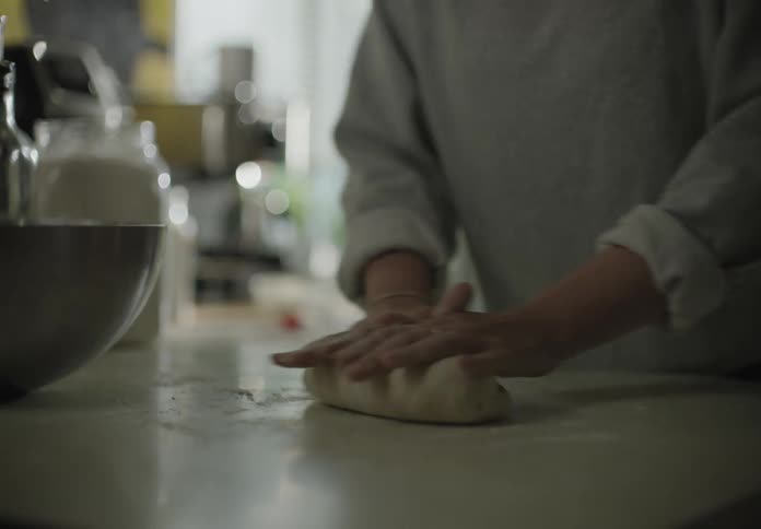 A white woman kneads a wad of dough in a kitchen