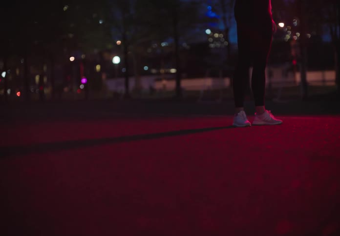 A white woman stands on a court in a park and bounces a ball