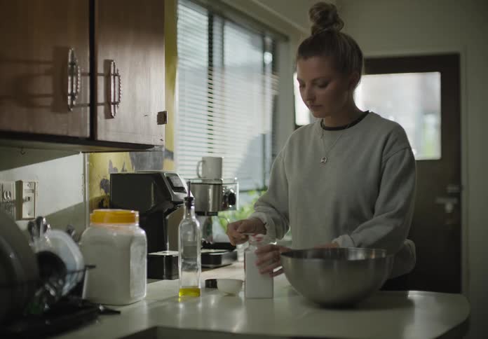 A white woman mixes various food items on a large metal bowl in a kitchen