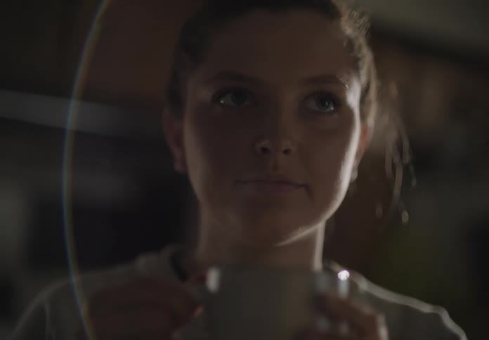 Female standing in kitchen smells the hot beverage she is holding with both hands then smiles and moves to put the mug down
