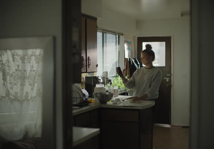 A woman in the kitchen kneading dough and video chatting on a smart phone