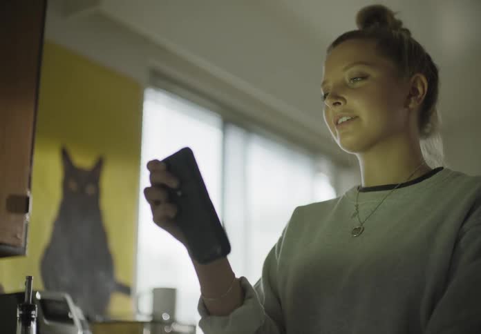 A woman kneads dough on a kitchen counter and then picks up her phone for a video call