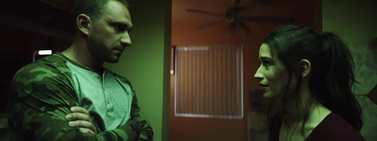 A man stands with his arms crossed looking at a woman speaking to him