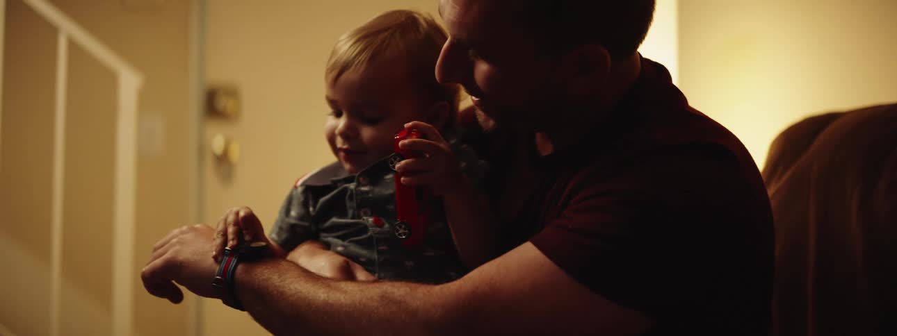 Son holding toy car is held by father and shown wristwatch