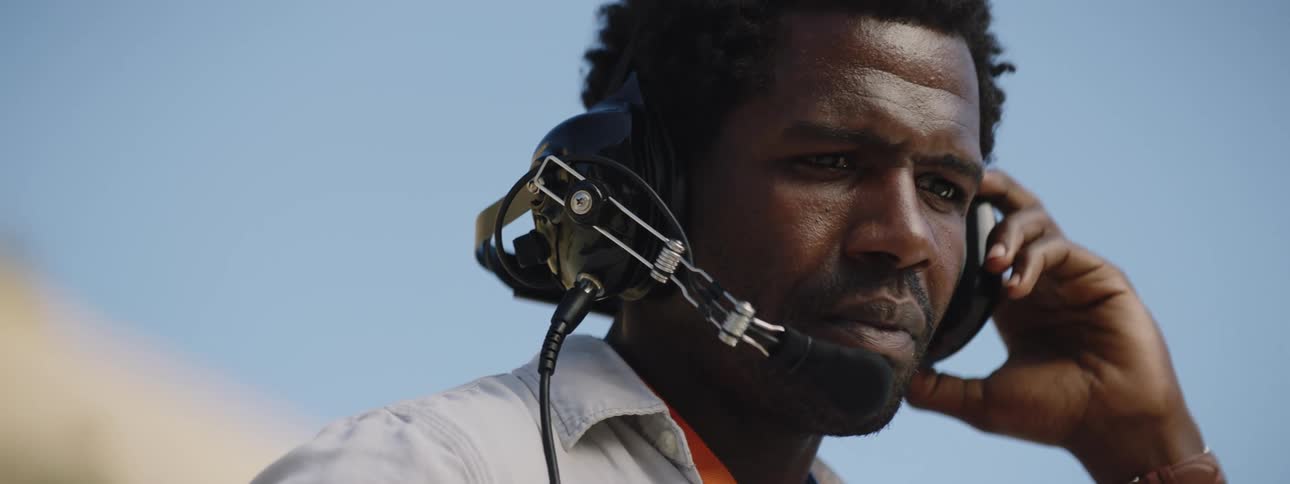 A black man stands outdoors talking over a headset
