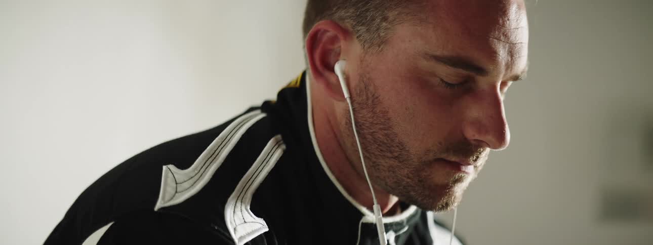 A white man listens to earbuds in a room