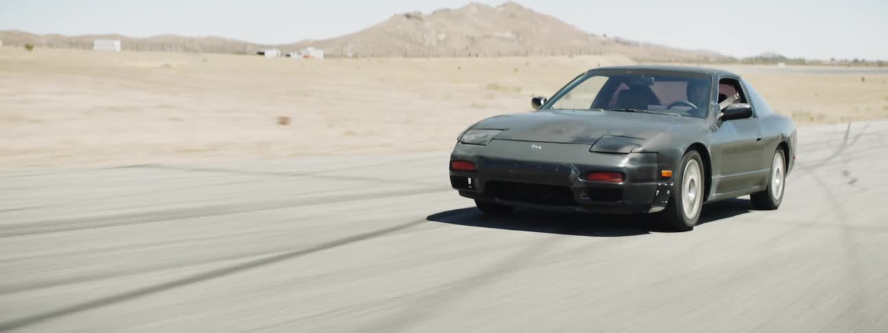 A person driving a car on a track in the desert during the day