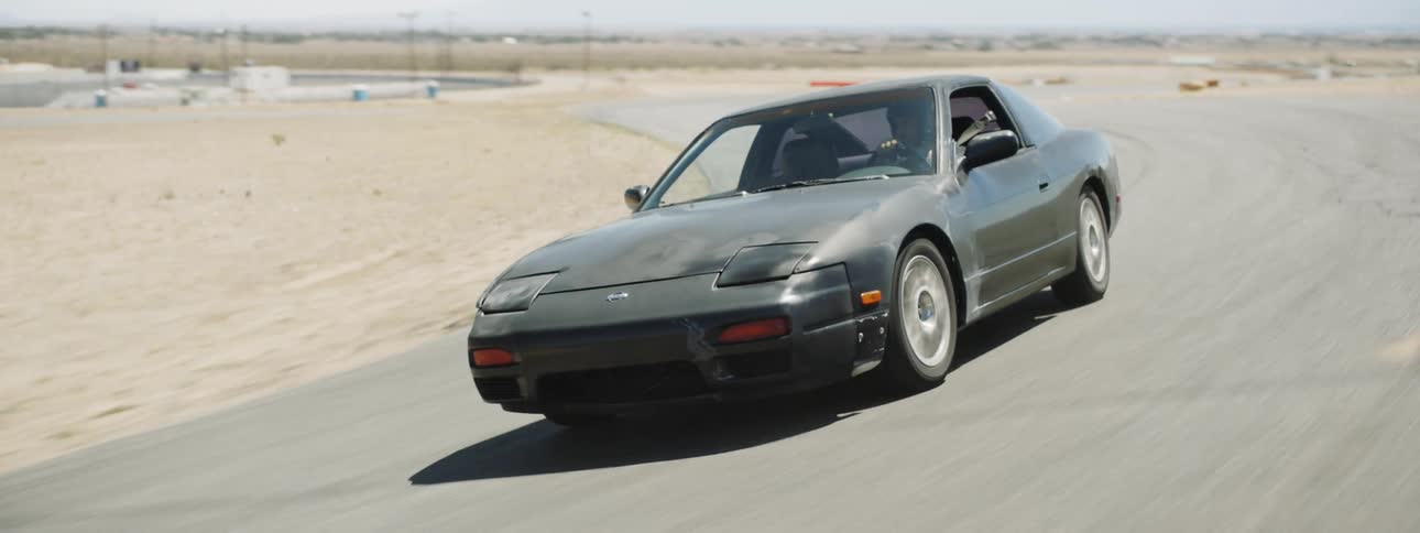 A driver races a sports car around a track in the desert