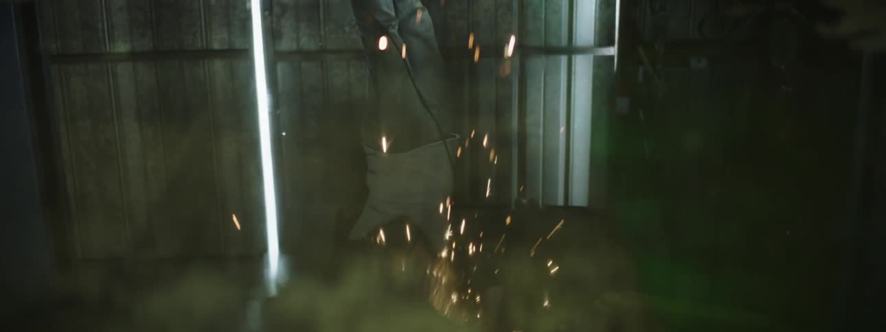 A man appears to hang upside down in order to use a cutter on a piece of metal