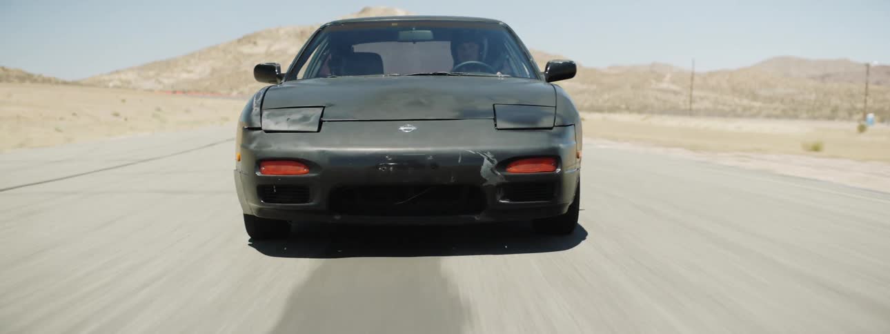 A racer drives a car at speed down a road through a desert
