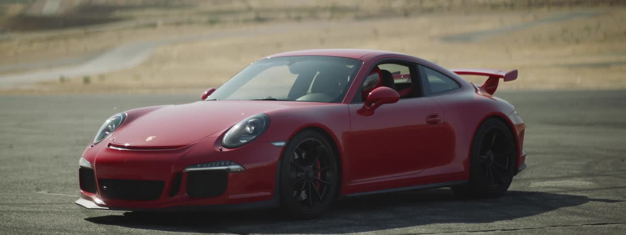 Sun glares off windshield of red sports car parked near scrub and mountain
