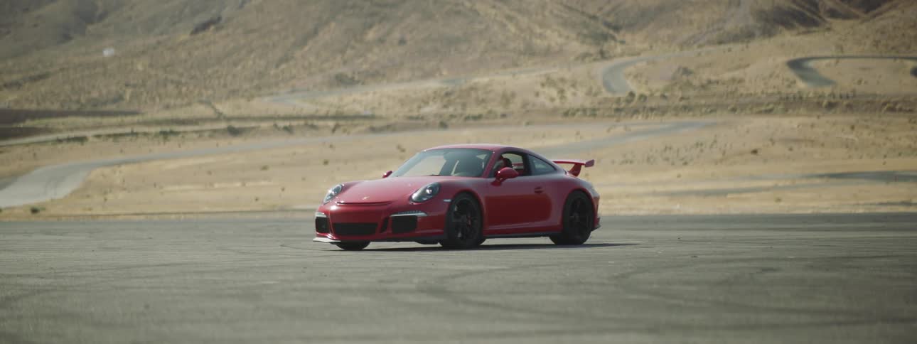 Driver wearing crash helmet sits in red sports car in lot near mountain