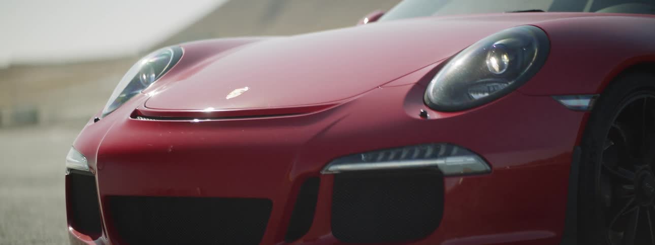 A red porsche parked on a track in the desert with the sun shining down on it