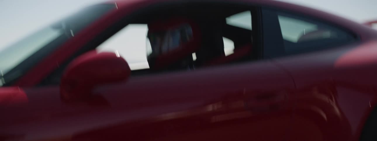 A professional driving a speeding sports card down a road in the countryside