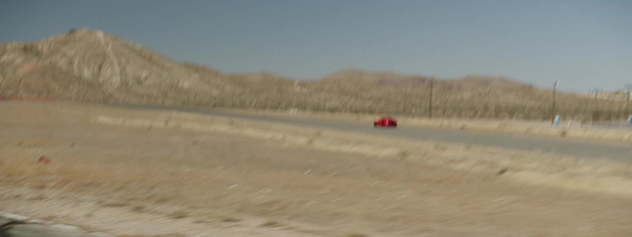 A red car tears off down a race track in a desert