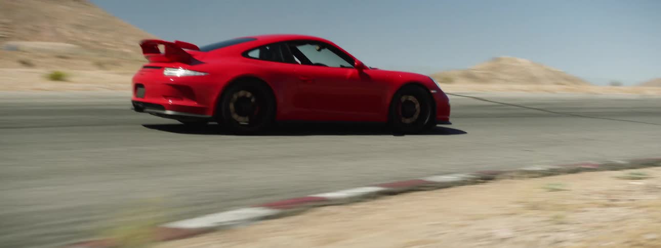 Red sports car races along road among scrub and mountains under a clear blue sky