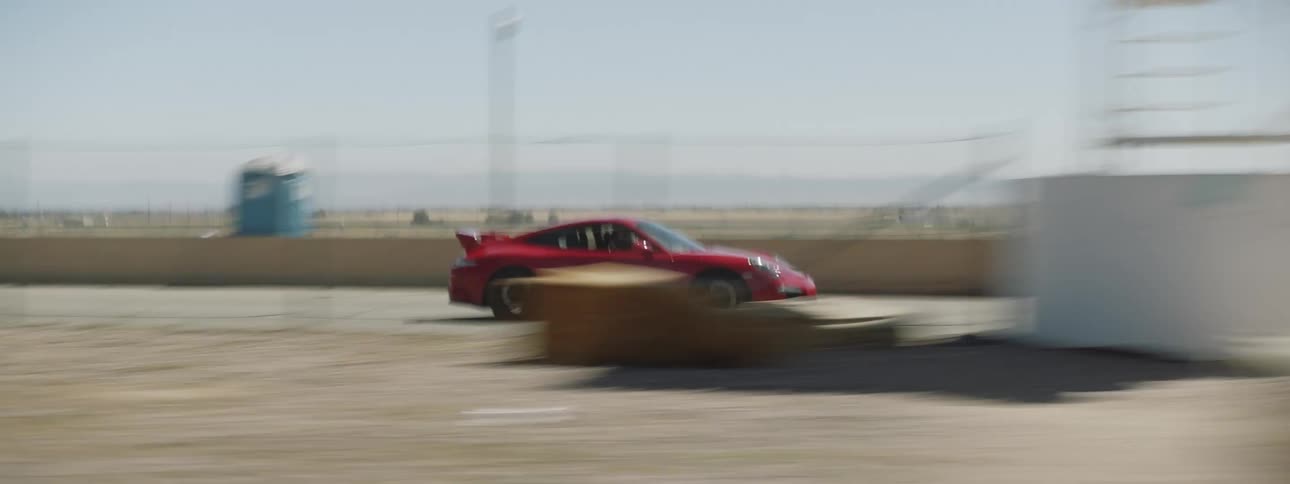 A red sports car races on an empty road with sand on either side