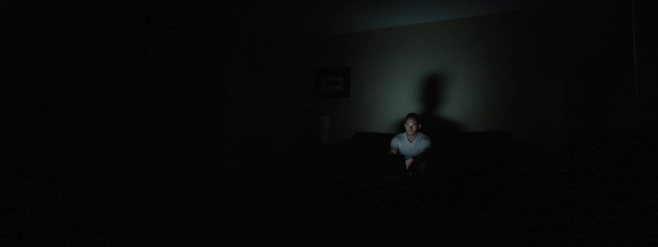 A white man sits alone in a room watching television in the dark