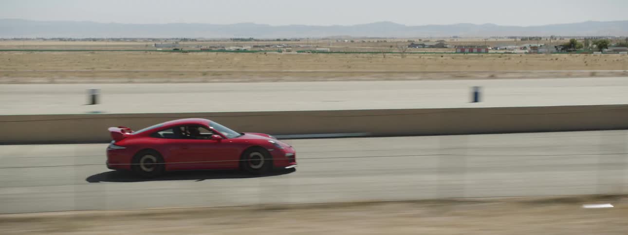 A red sports car races on an empty desert track