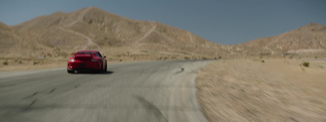 A red sports car races around a turn on an empty desert road
