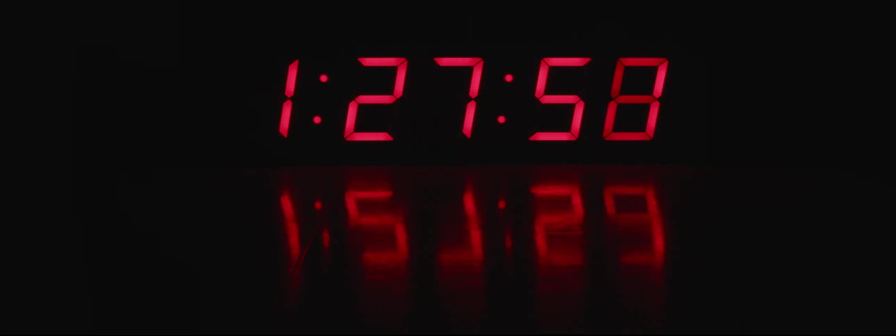 A digital clock speeds forward glowing numbers against black with a reflection on the surface