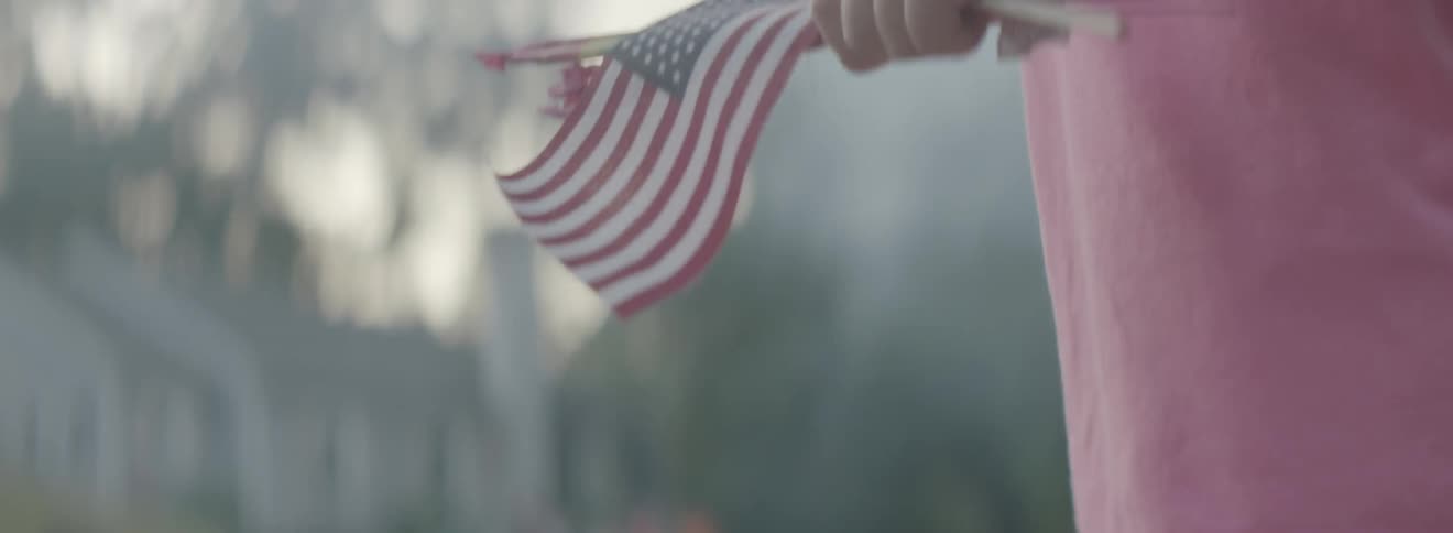 A girl holds a burning sparkler and american flag outside in the summer