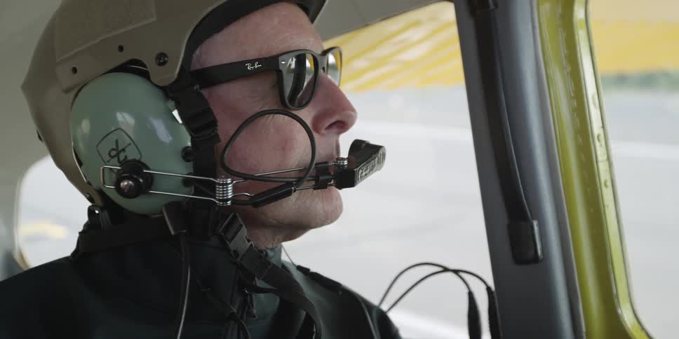 A man wearing a helmet looks out of a plane window