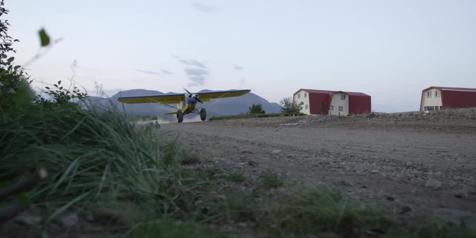 A plan slowly takes off on a dirt road by some homes