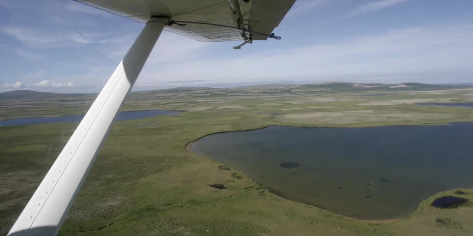 The wing of a small plane seen as it flies over an area with two small lakes