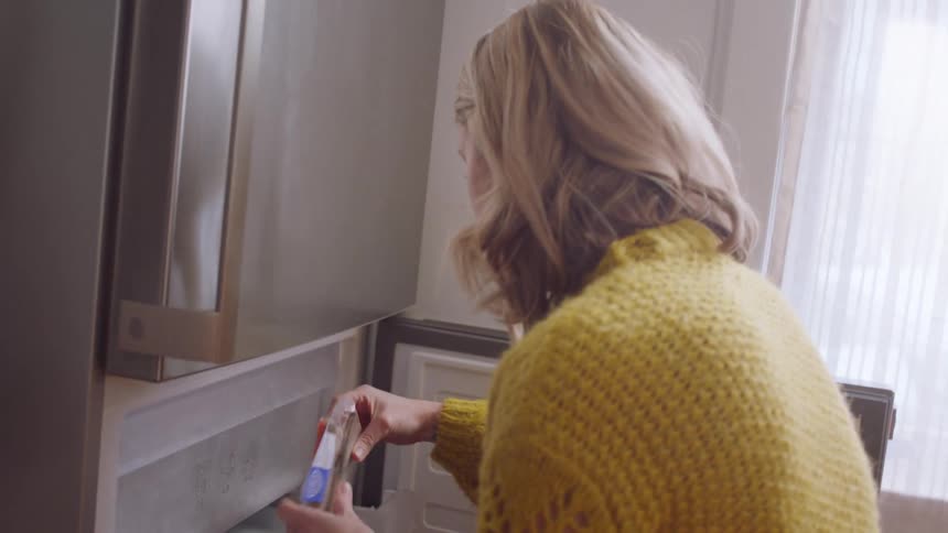 Woman puts bags of food on the fridge in her kitchen