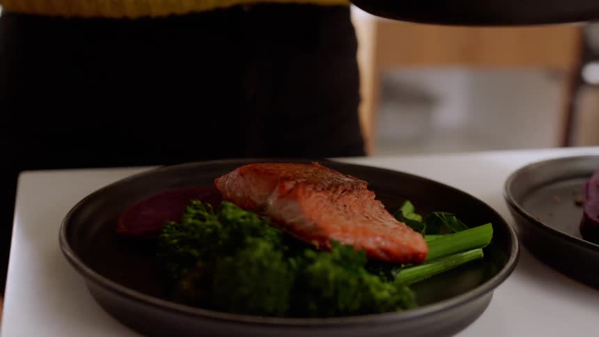 A woman garnishes two plates of salmon and broccoli on the kitchen counter