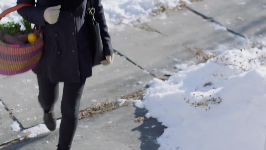 Woman carries basket of fresh produce up steps to home