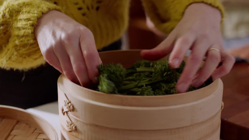 A woman puts broccoli in a container to cook