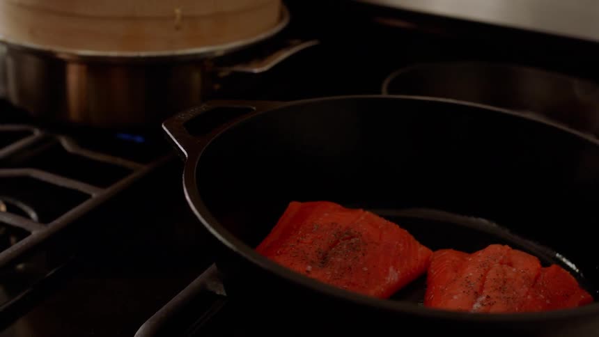 Person places fish fillets in iron skillet on stove