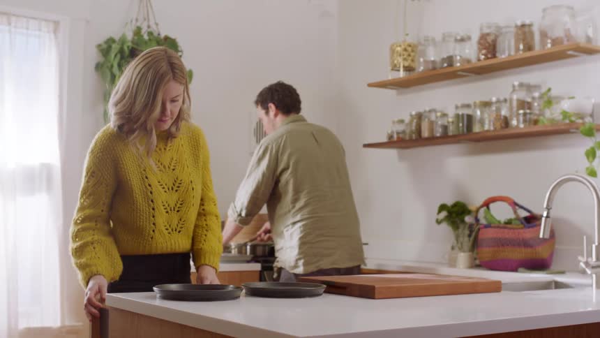 A man and woman preparing food and dishes in a kitchen