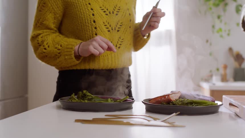 A man places pieces of salmon on top of steamed broccoli for him and his wife
