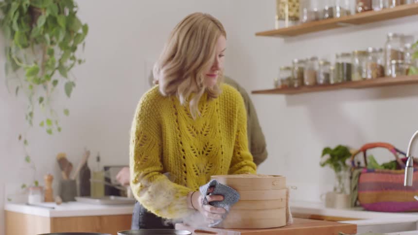 Woman places a bamboo container on the counter as a man stands near a stove behind her