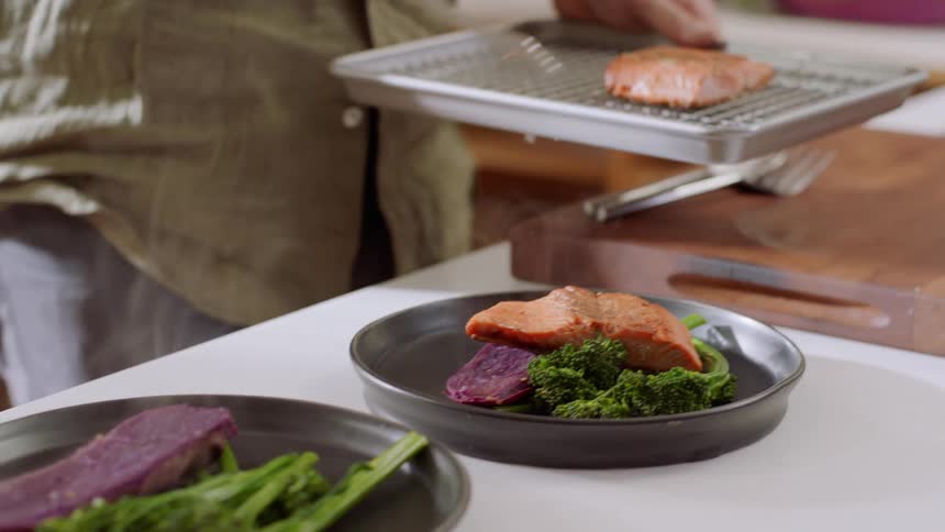 A man serves fish onto two plates in a home kitchen