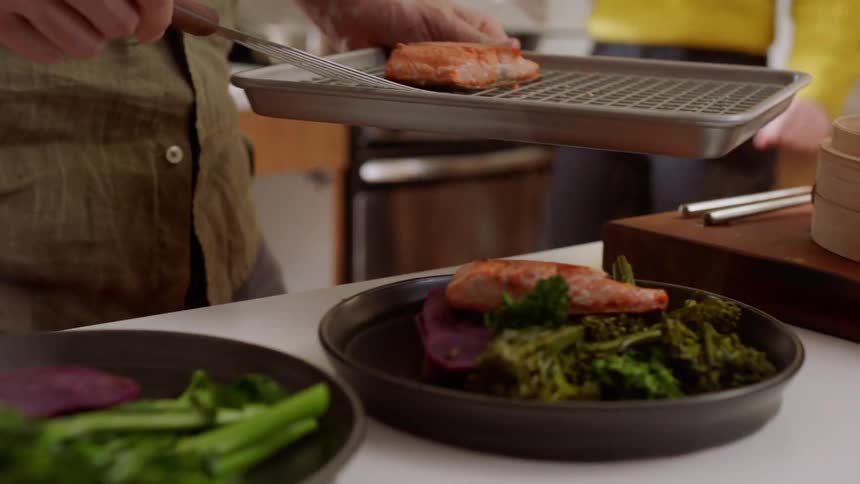 Man placing cooked fish on plate with broccoli