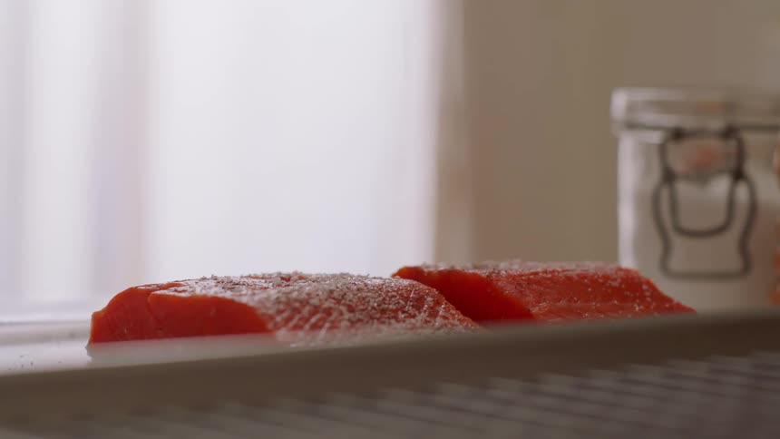 Sliced salmon being salted on the counter top of a kitchen