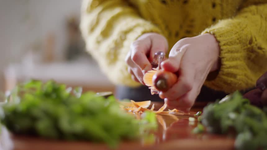 A white woman shreds a carrot in a kitchen