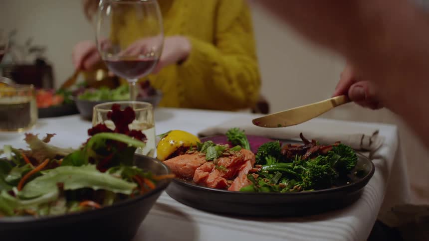 Two people sit at table eating fish fillets and salad