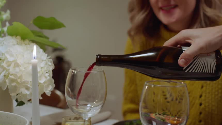 A man pours a glass of red wine for his wife as they sit down to eat dinner