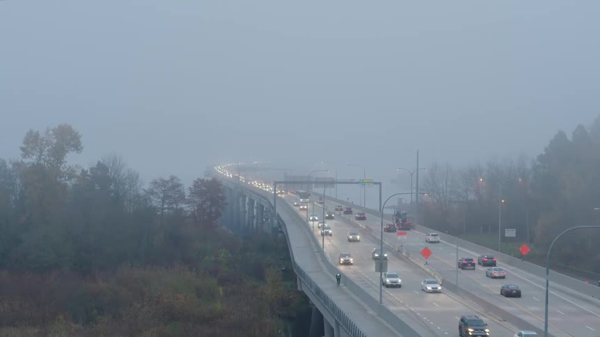 Cars travel in both directions on a bridge on a foggy day